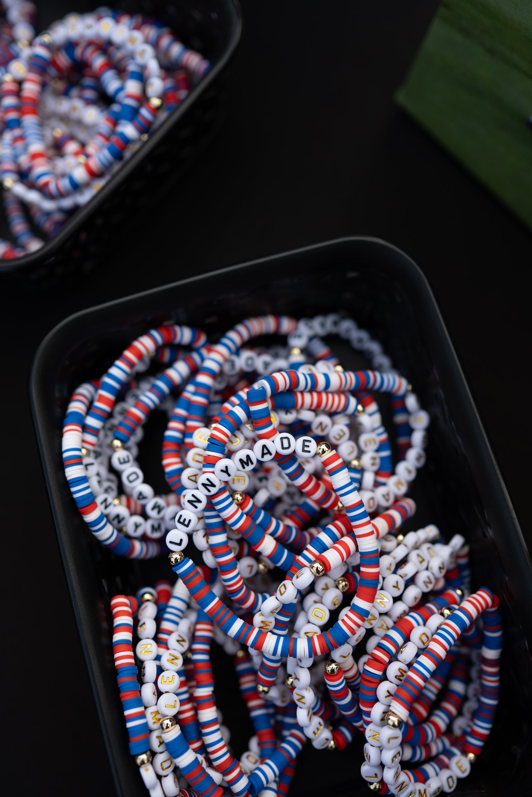 Close-up of red, white and blue beaded LENNYMADE bracelets arranged in black trays.