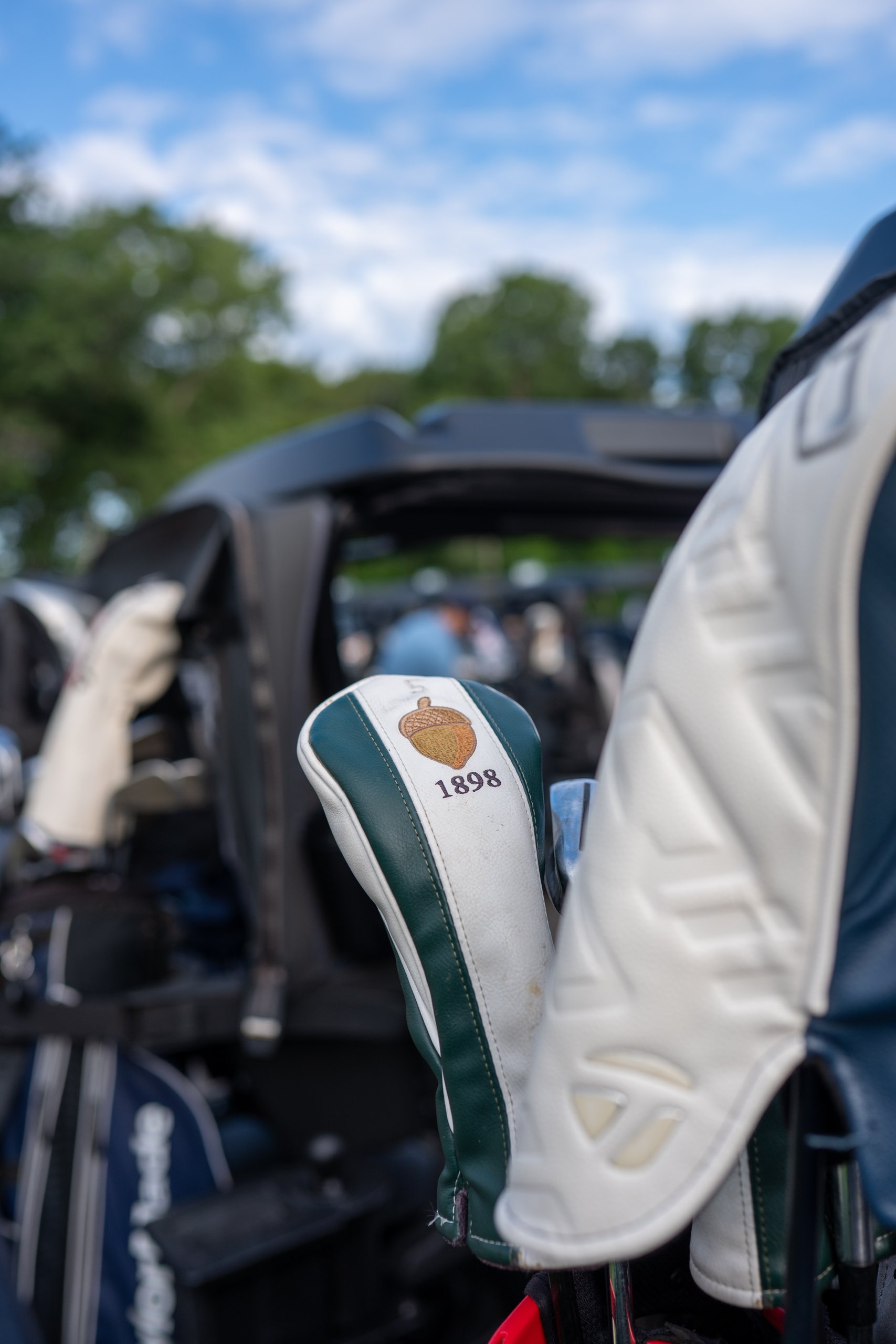 Close-up of a golf club headcover embroidered with an acorn and 1898 tucked among bags on the carts.