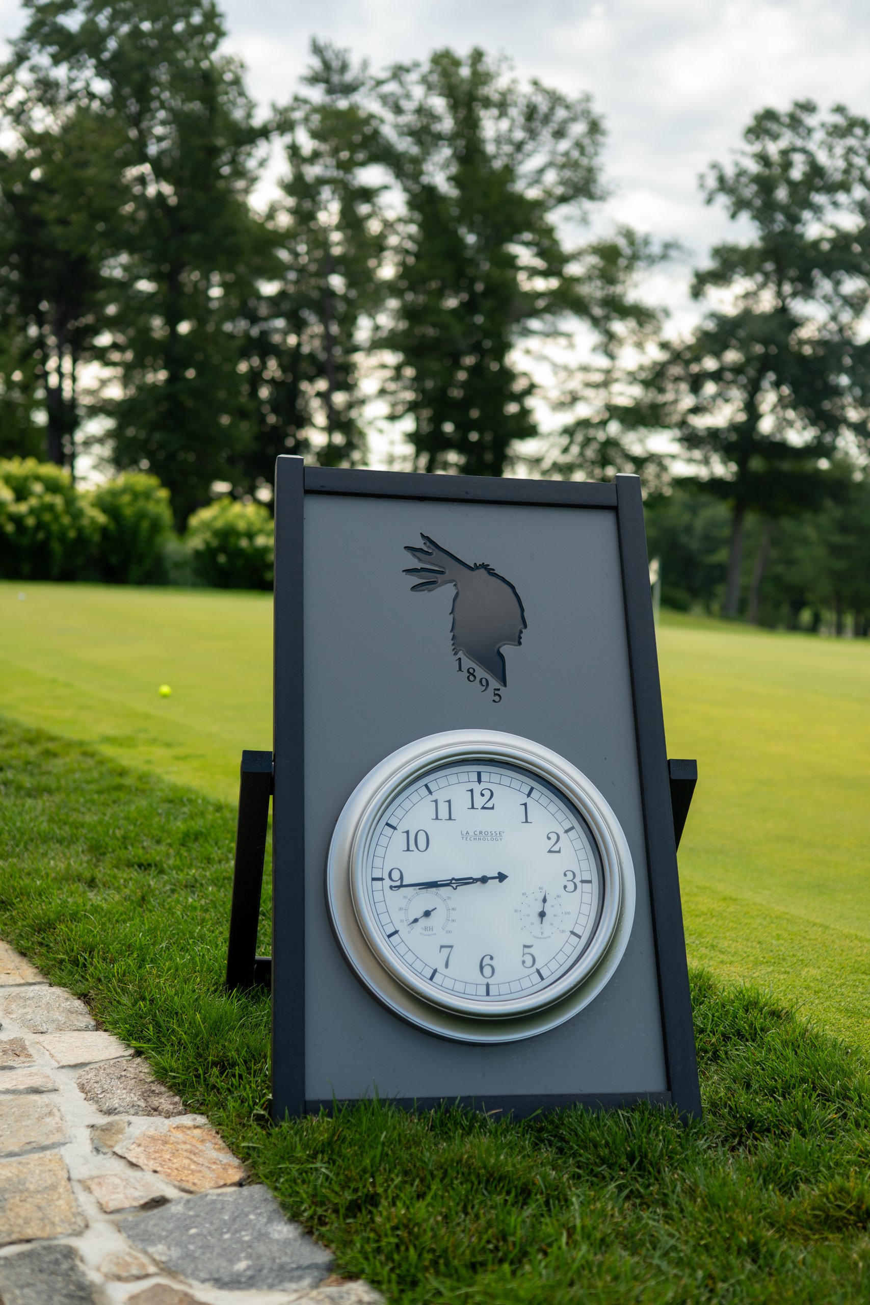The club's starter sign on the lawn with its 1895 emblem and a large clock and thermometer beside the practice area.