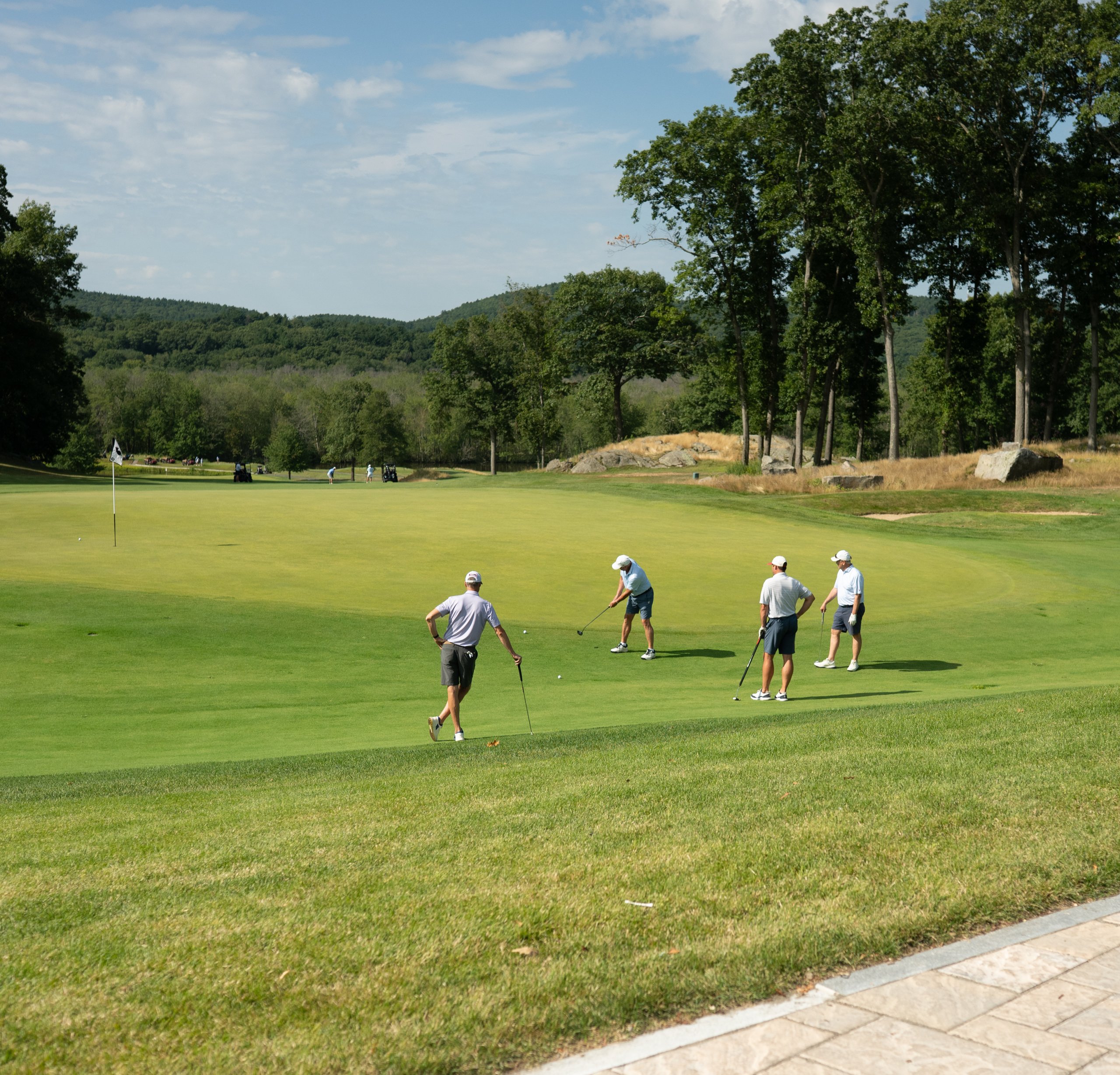 Foursome putting out on the green with the flag to the left and a sweeping view of the tree-covered hills beyond.
