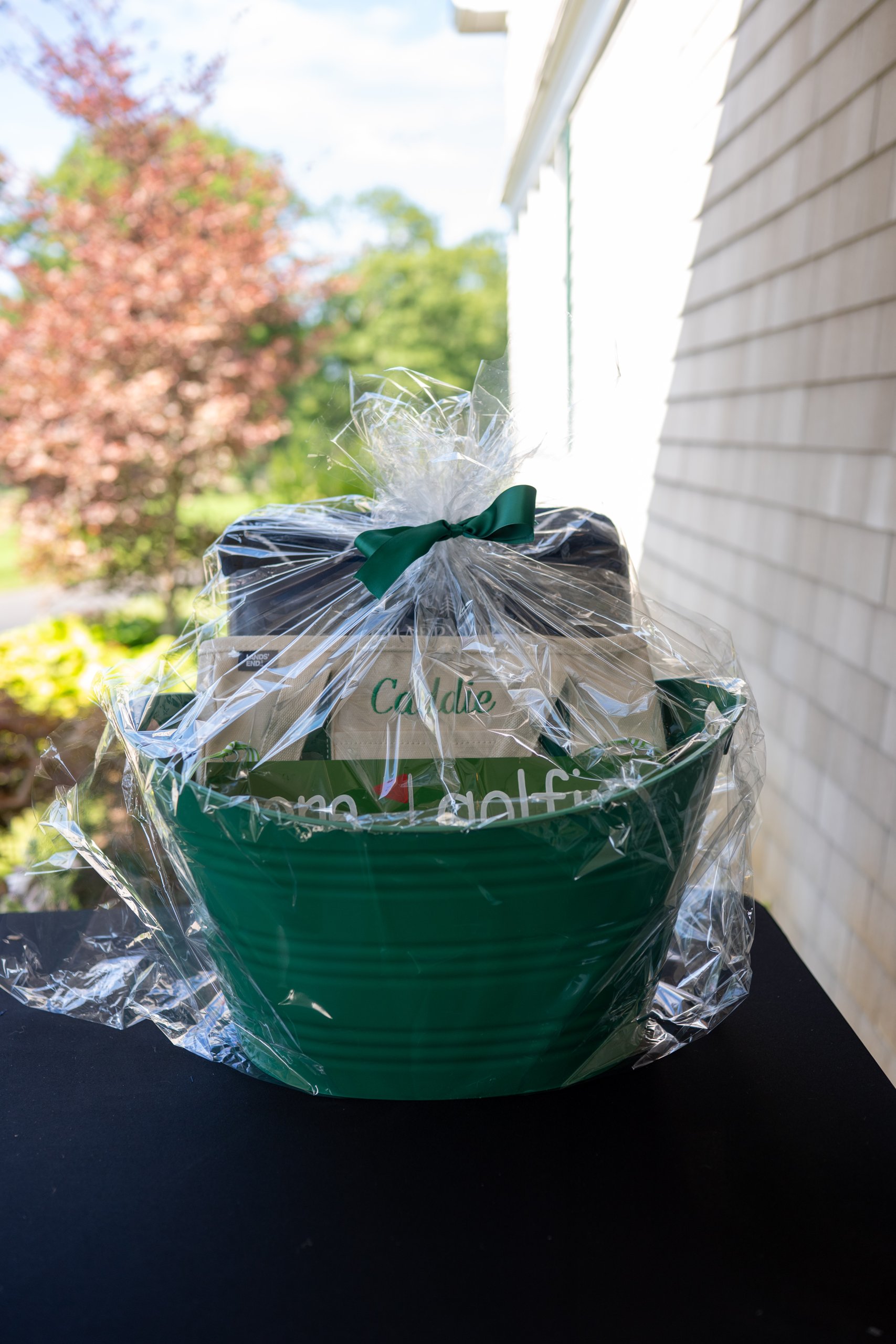 A golf-themed raffle basket in a green bin with a monogrammed Caddie tote, wrapped in cellophane with a green bow.