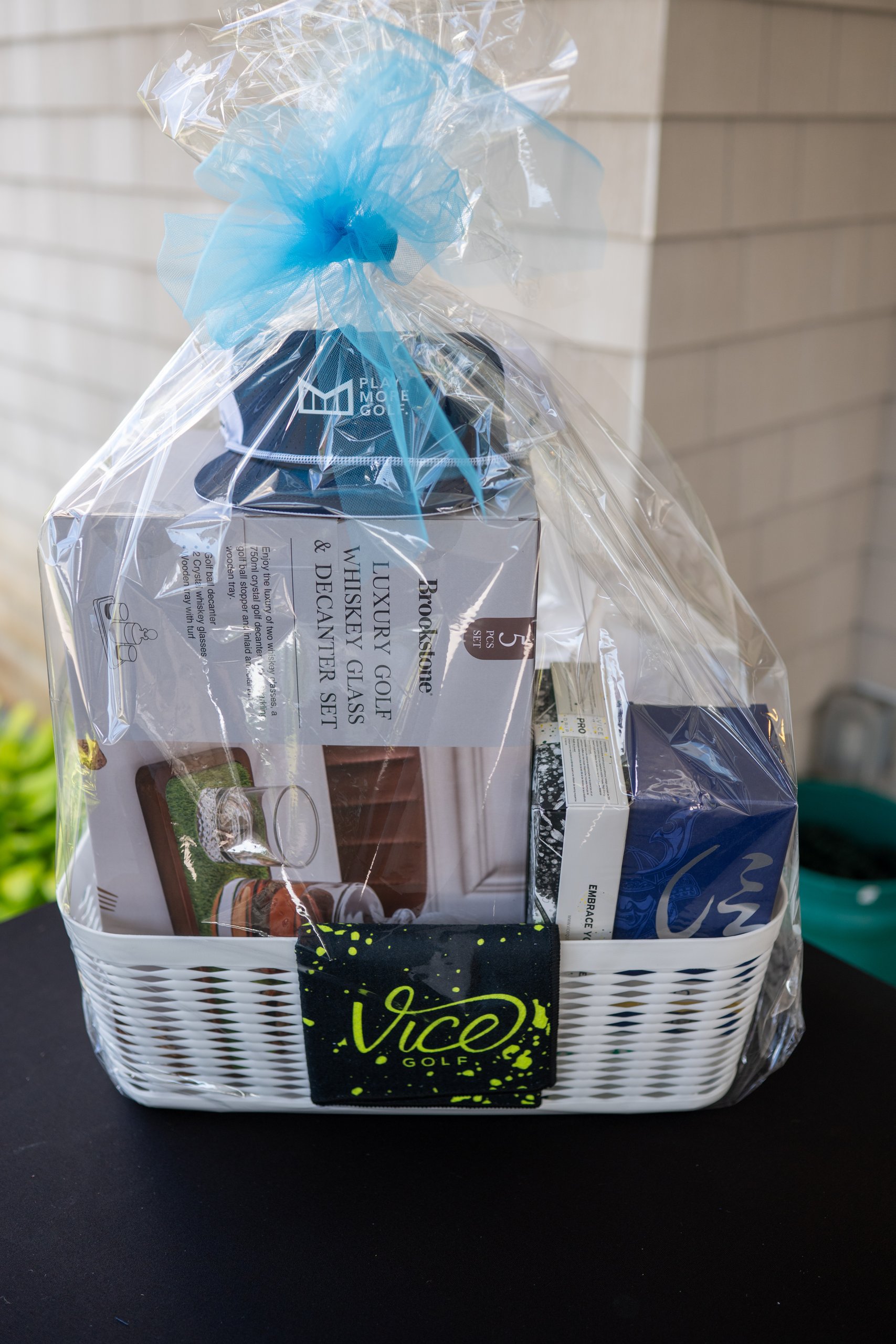 Raffle basket featuring a Brookstone luxury golf whiskey glass and decanter set and a Vice Golf towel, tied with a blue bow.