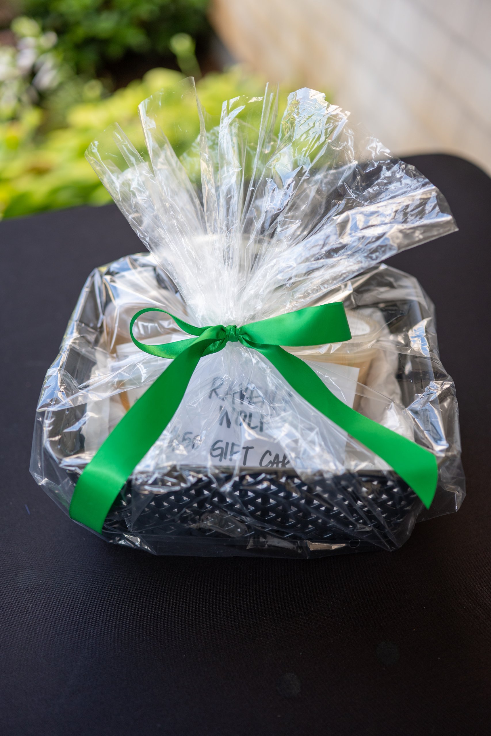 A cellophane-wrapped raffle basket holding a Raven & Wolf gift card, finished with a green bow.