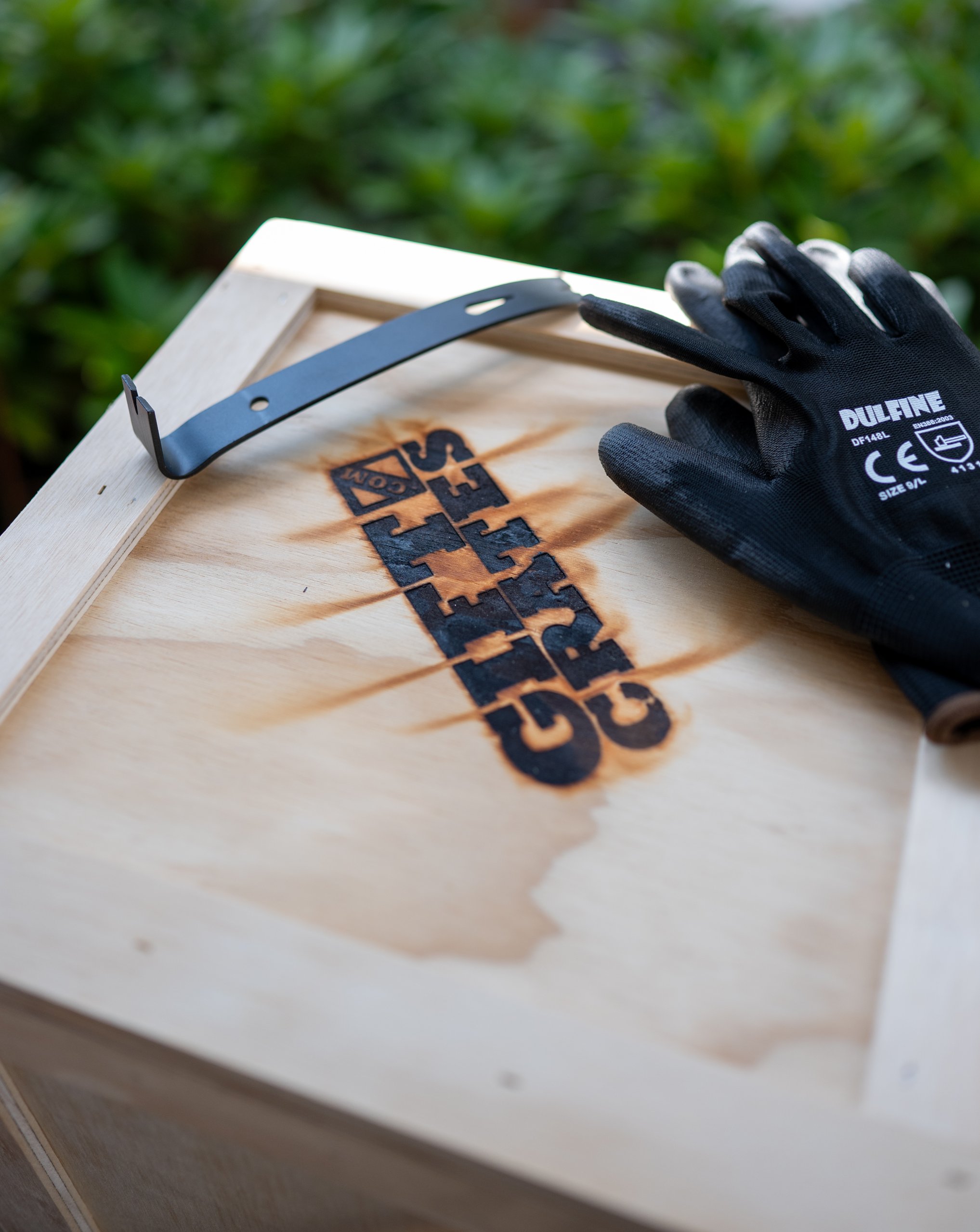 A wood crate lid with a branded logo and a metal handle, work gloves resting on top during setup.