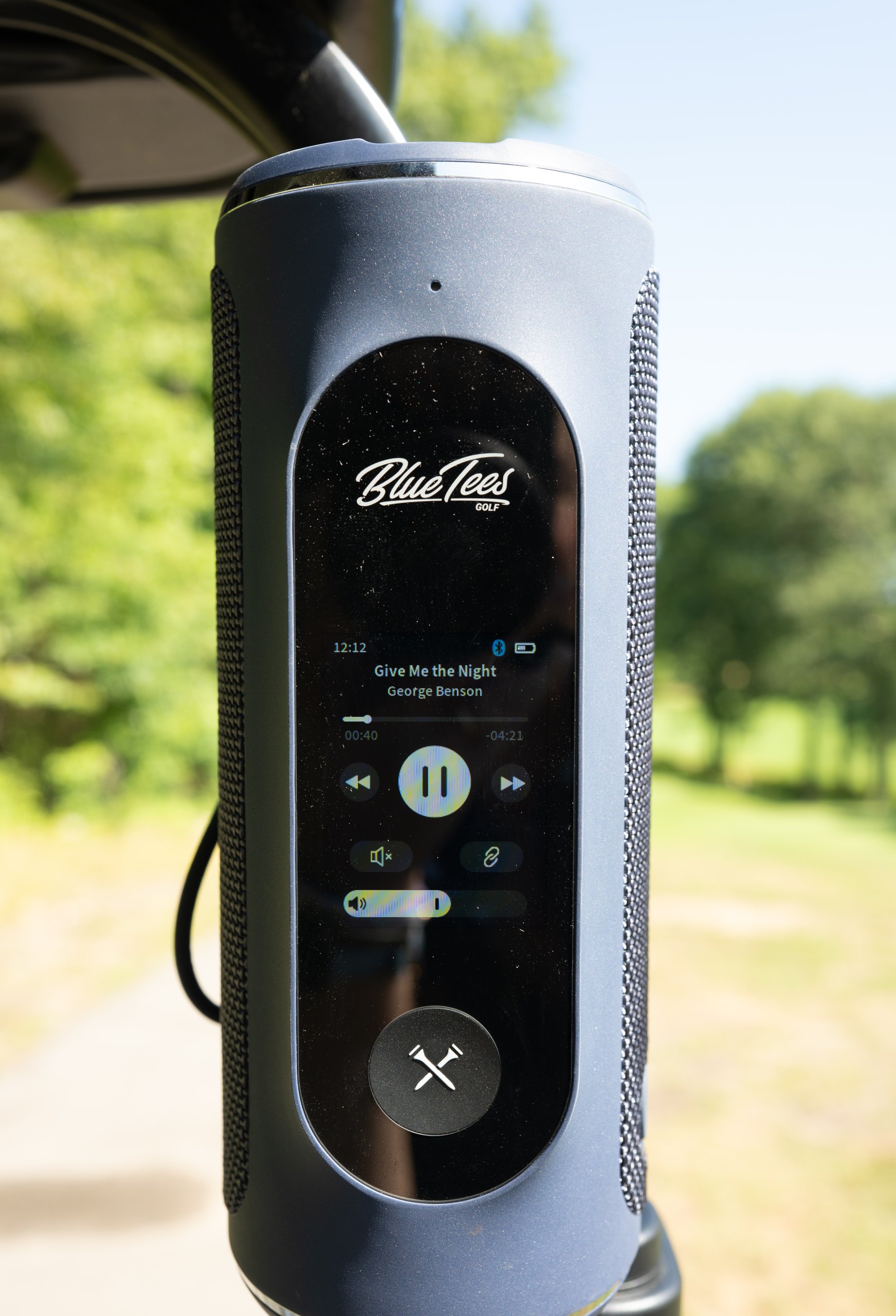 A Blue Tees Golf Bluetooth speaker clipped to the cart, its screen playing Give Me the Night by George Benson.