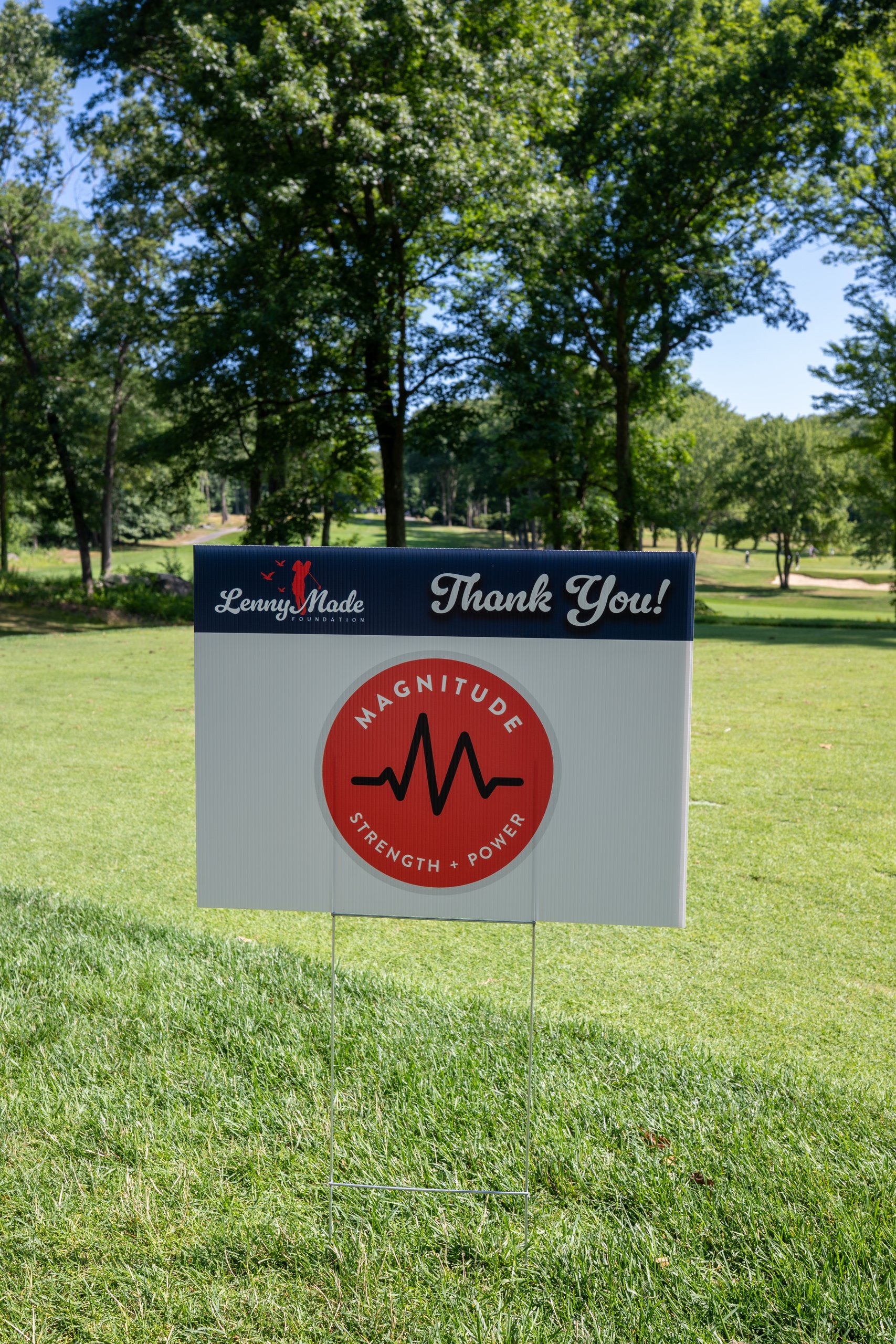 A LennyMade Foundation Thank You sponsor sign for Magnitude Strength and Power staked on the fairway.