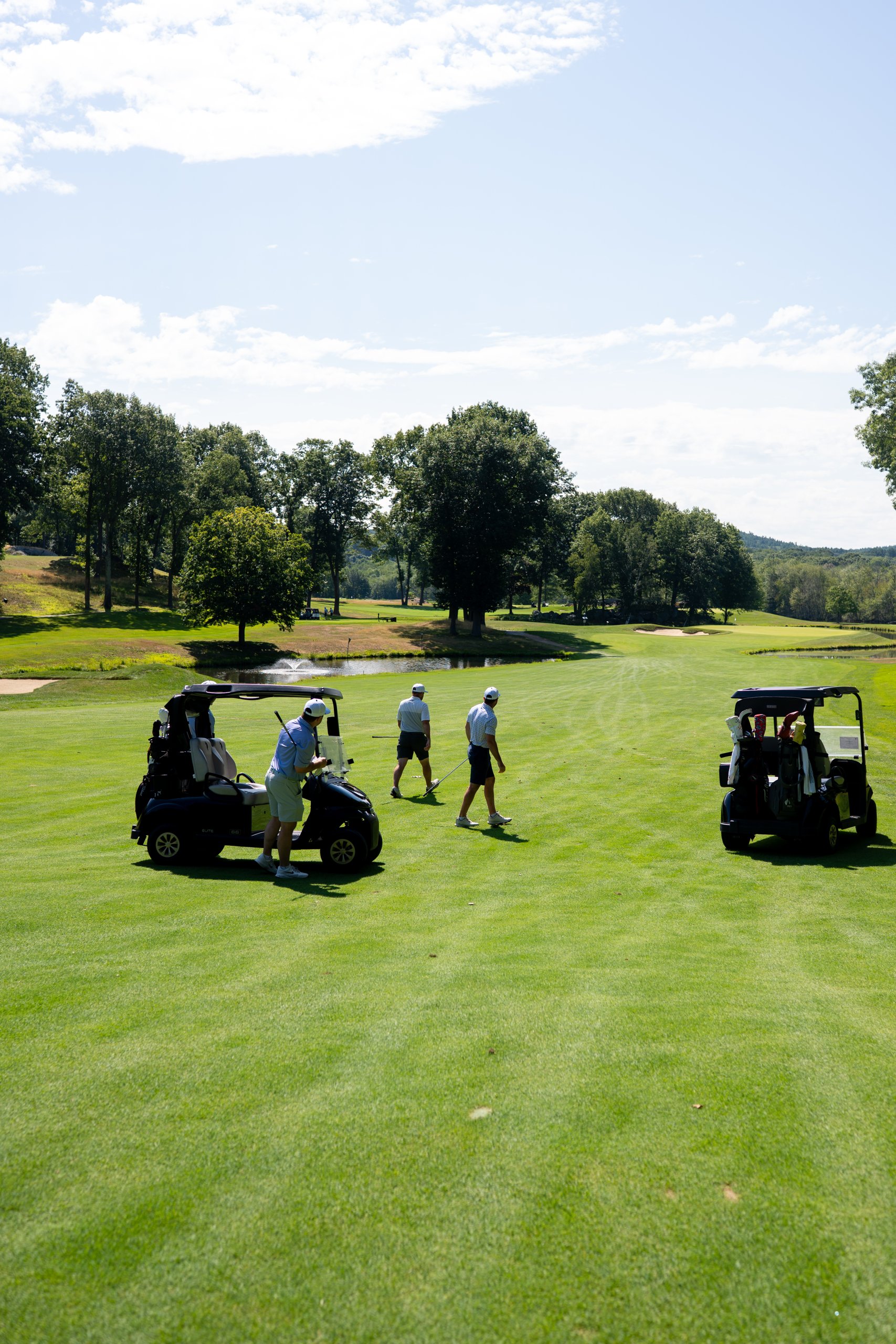 Foursome walking up the fairway with their two carts toward a fountain pond and green ahead.