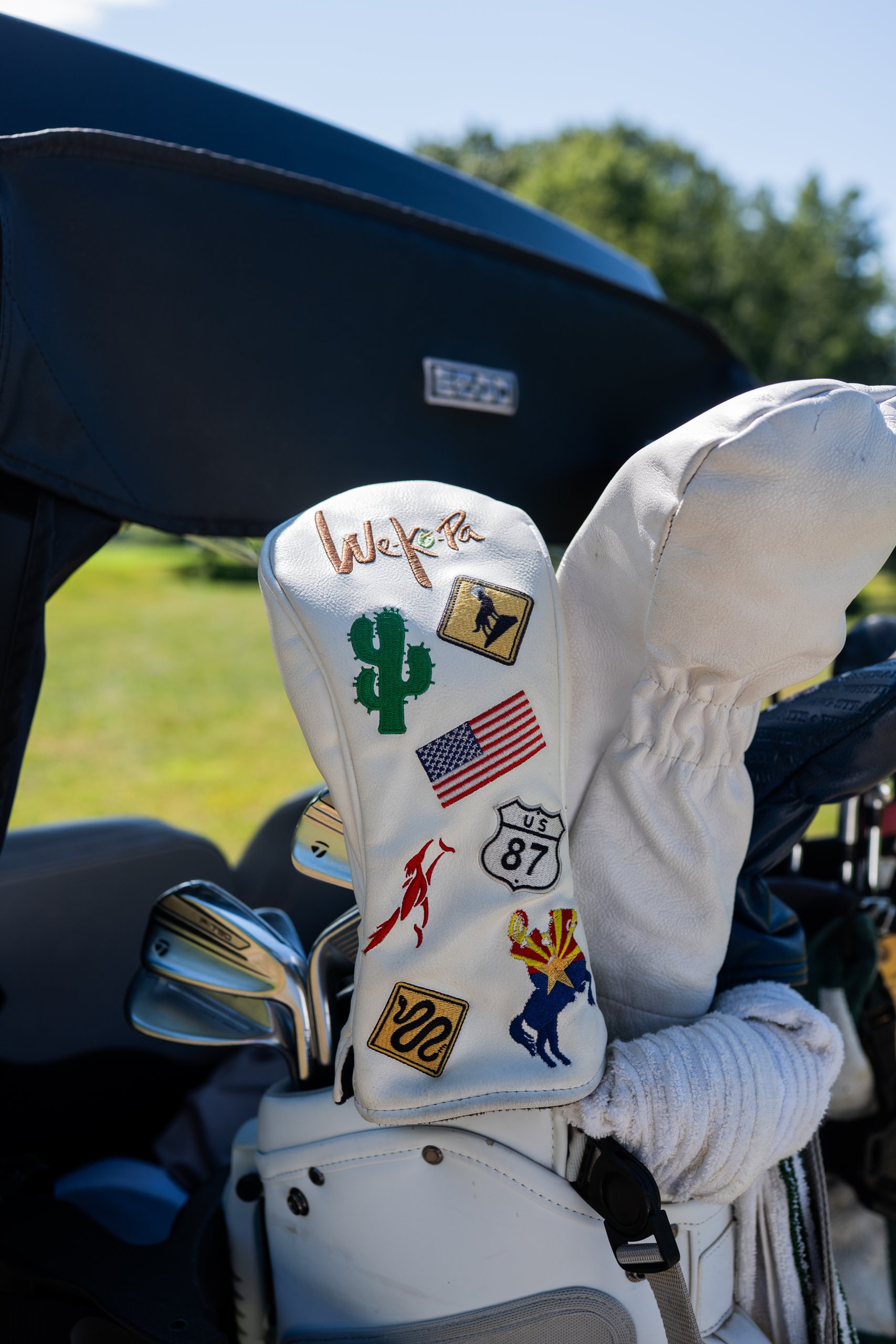 Close-up of a white We-Ko-Pa leather driver headcover covered in cactus, US flag and Arizona patches on a golf bag.
