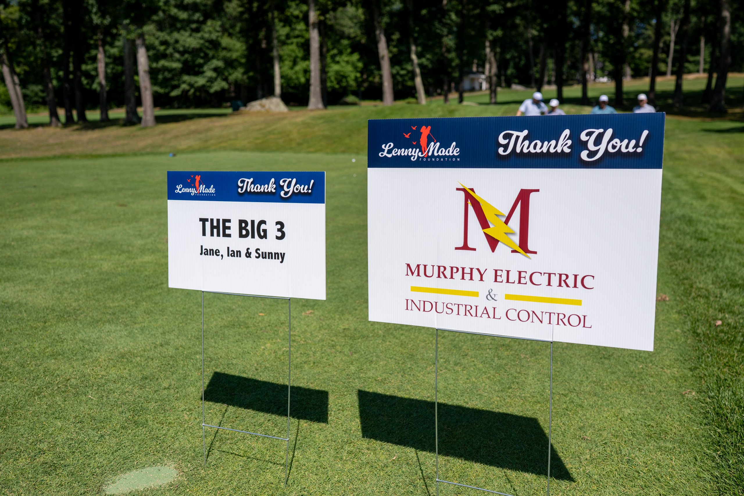 Two LennyMade Foundation sponsor signs on the fairway: The Big 3 (Jane, Ian and Sunny) and Murphy Electric and Industrial Control.