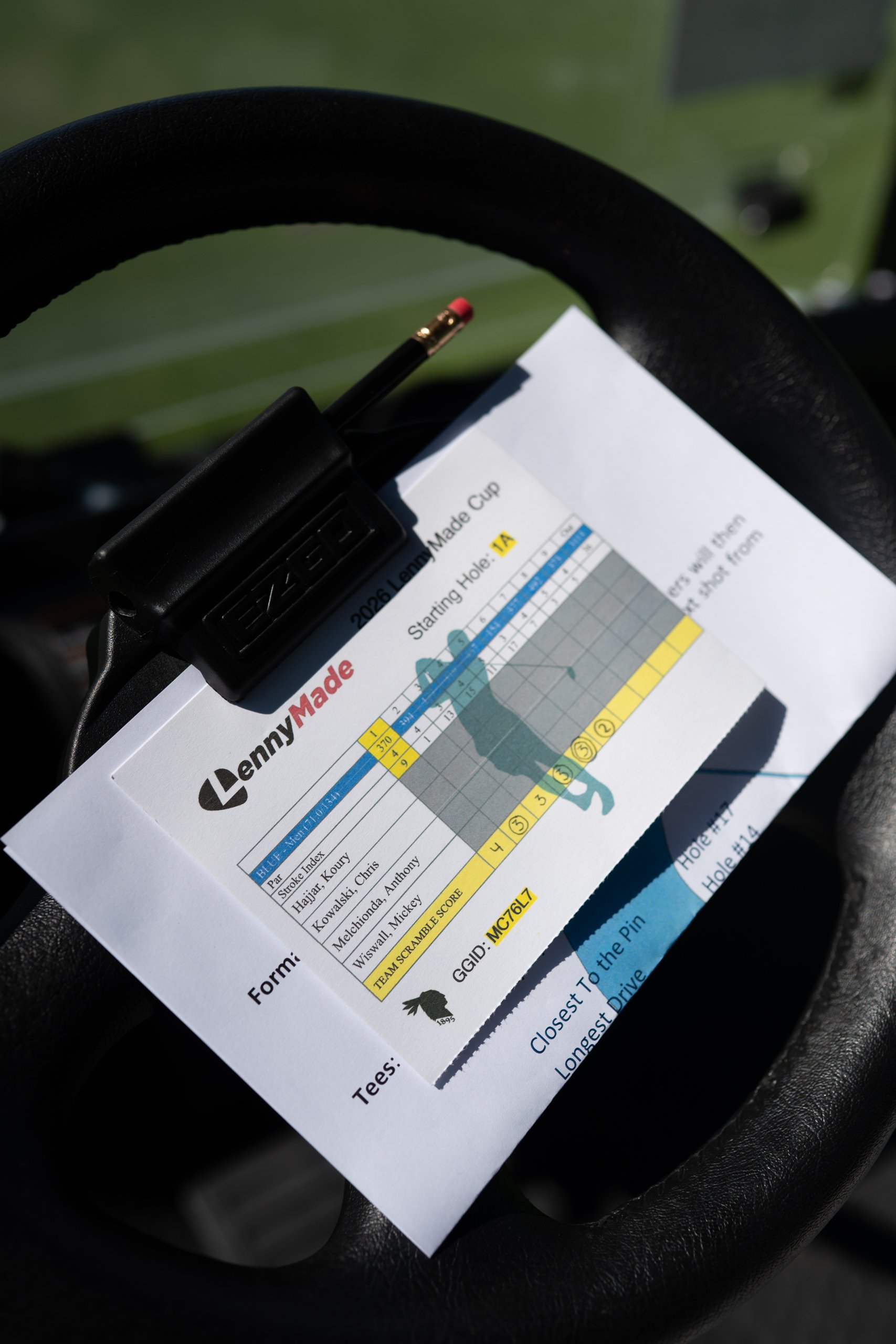 Close-up of a LennyMade Cup team scorecard and pencil clipped to the cart steering wheel with the starting hole and team GGID.