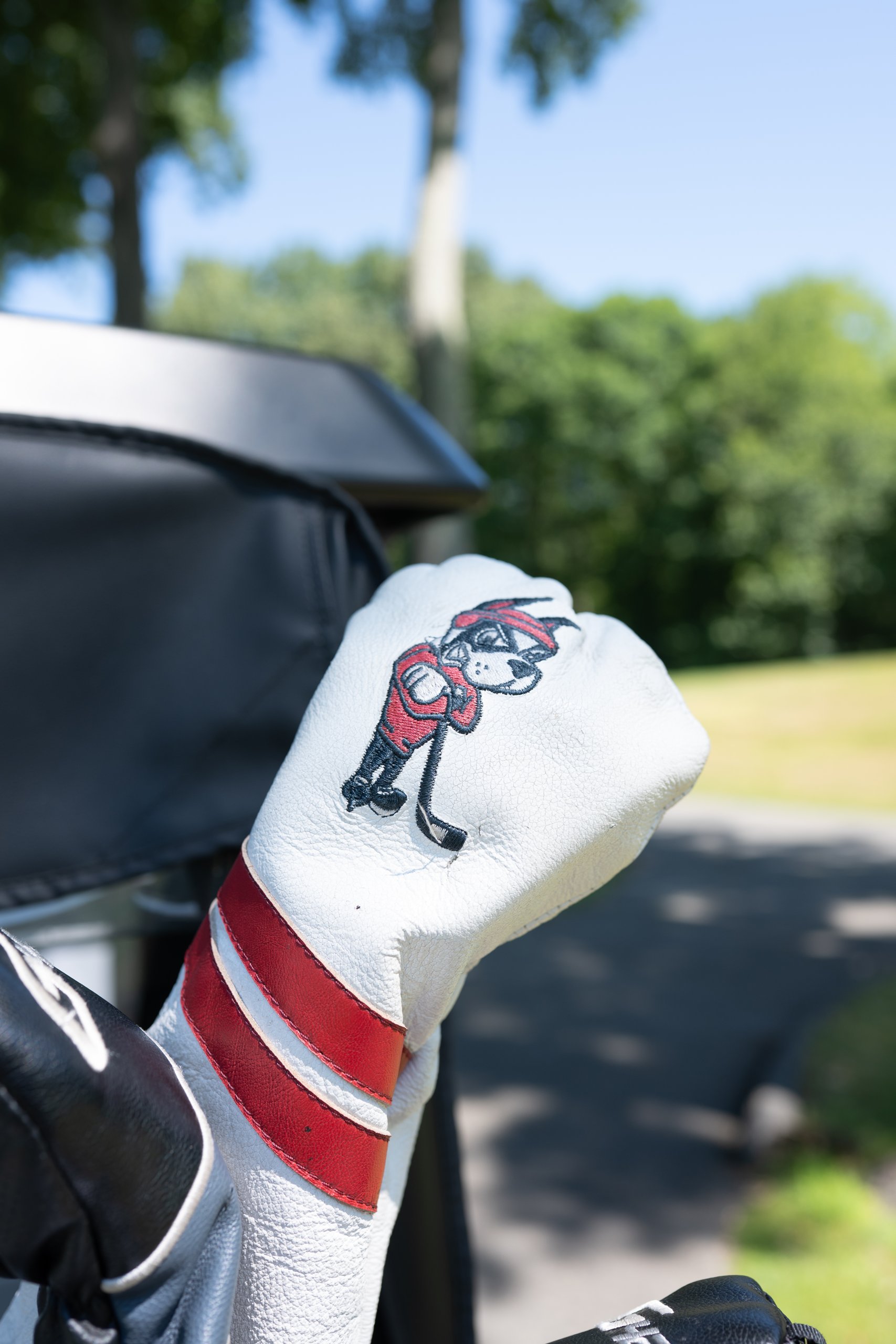 A white leather driver headcover embroidered with a red and navy terrier mascot and red stripes on a golf bag.