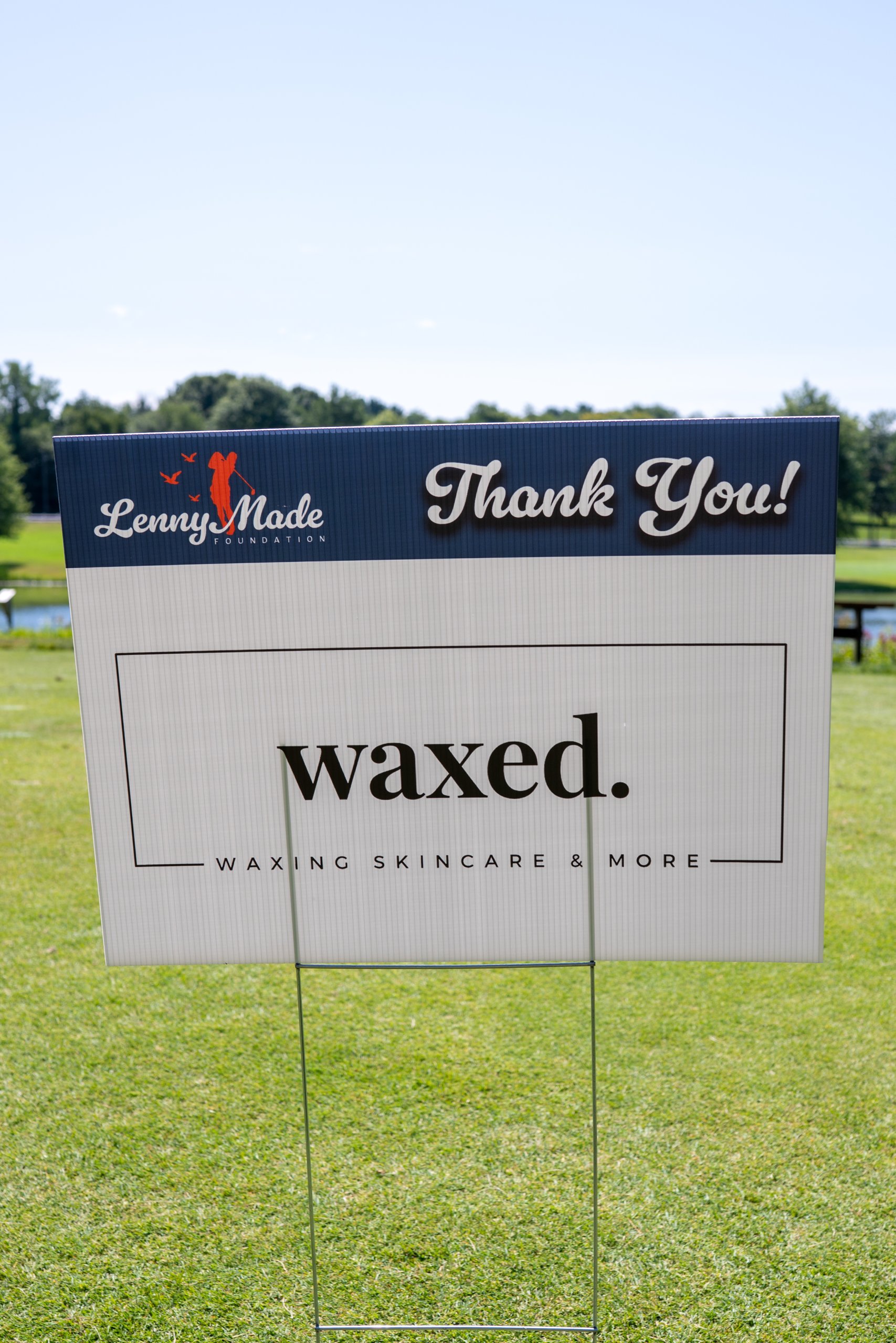 A LennyMade Foundation Thank You sponsor sign for Waxed, Waxing Skincare and More, with a pond behind.