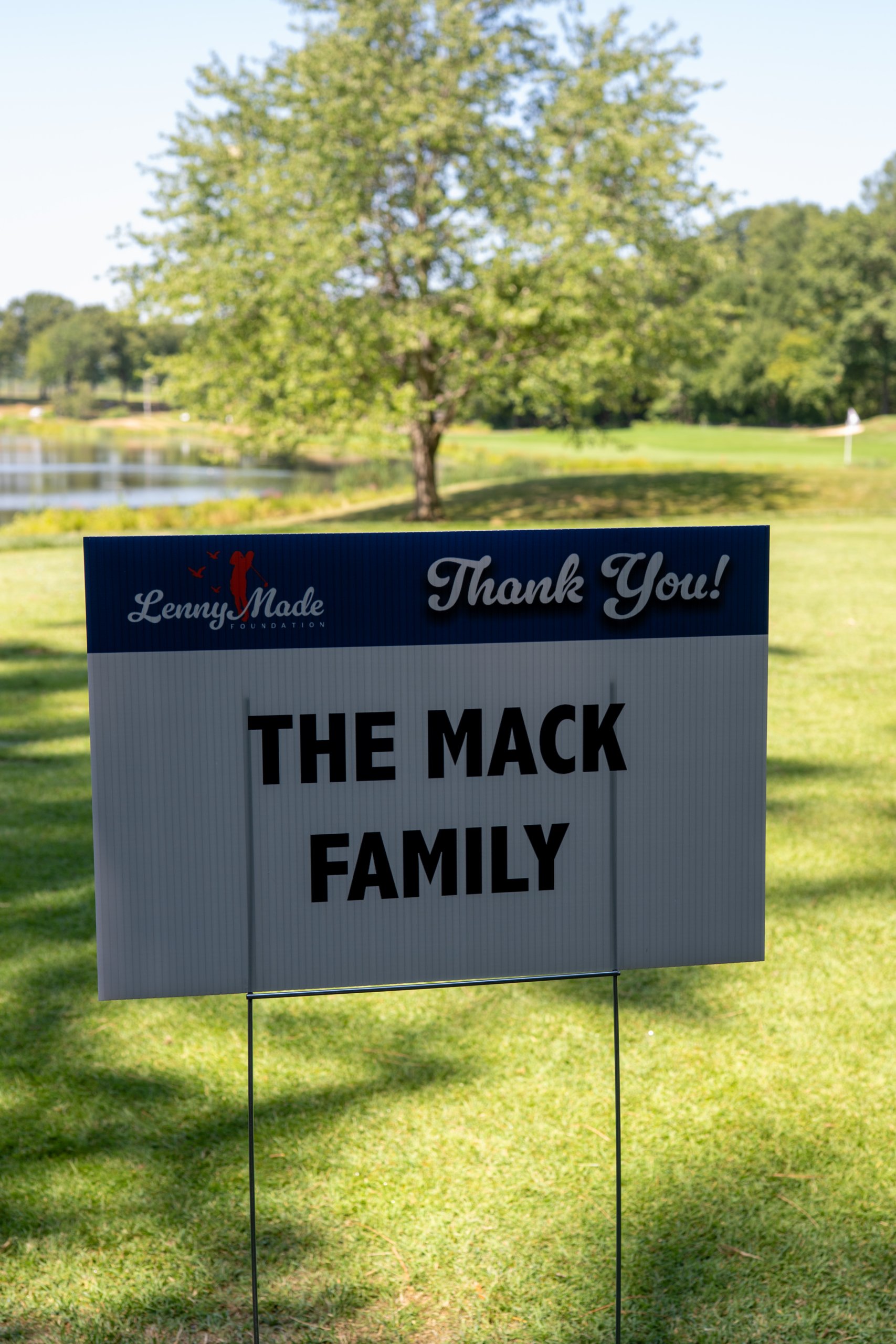 A LennyMade Foundation Thank You sponsor sign for The Mack Family, a pond and green behind.