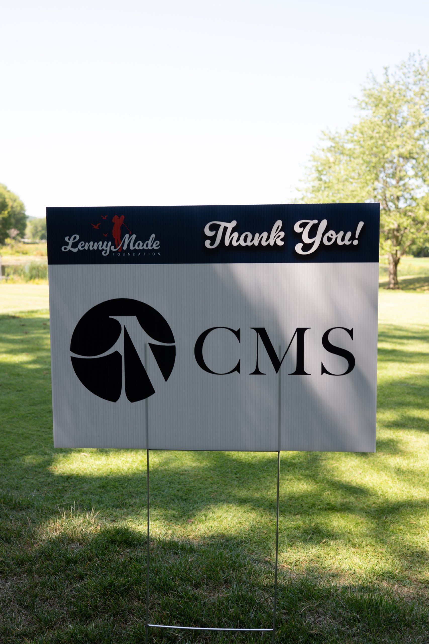 A LennyMade Foundation Thank You sponsor sign for CMS staked on the fairway.
