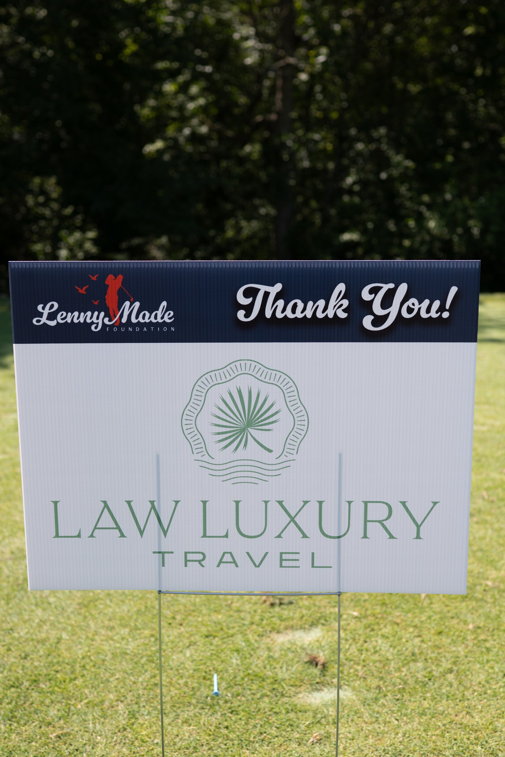 A LennyMade Foundation Thank You sponsor sign for Law Luxury Travel with its palm-leaf logo.