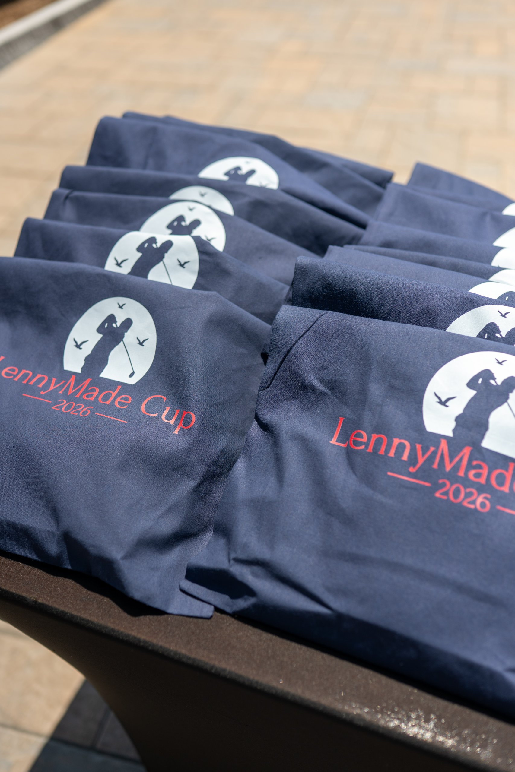 Folded navy LennyMade Cup 2026 t-shirts stacked on a table at check-in.