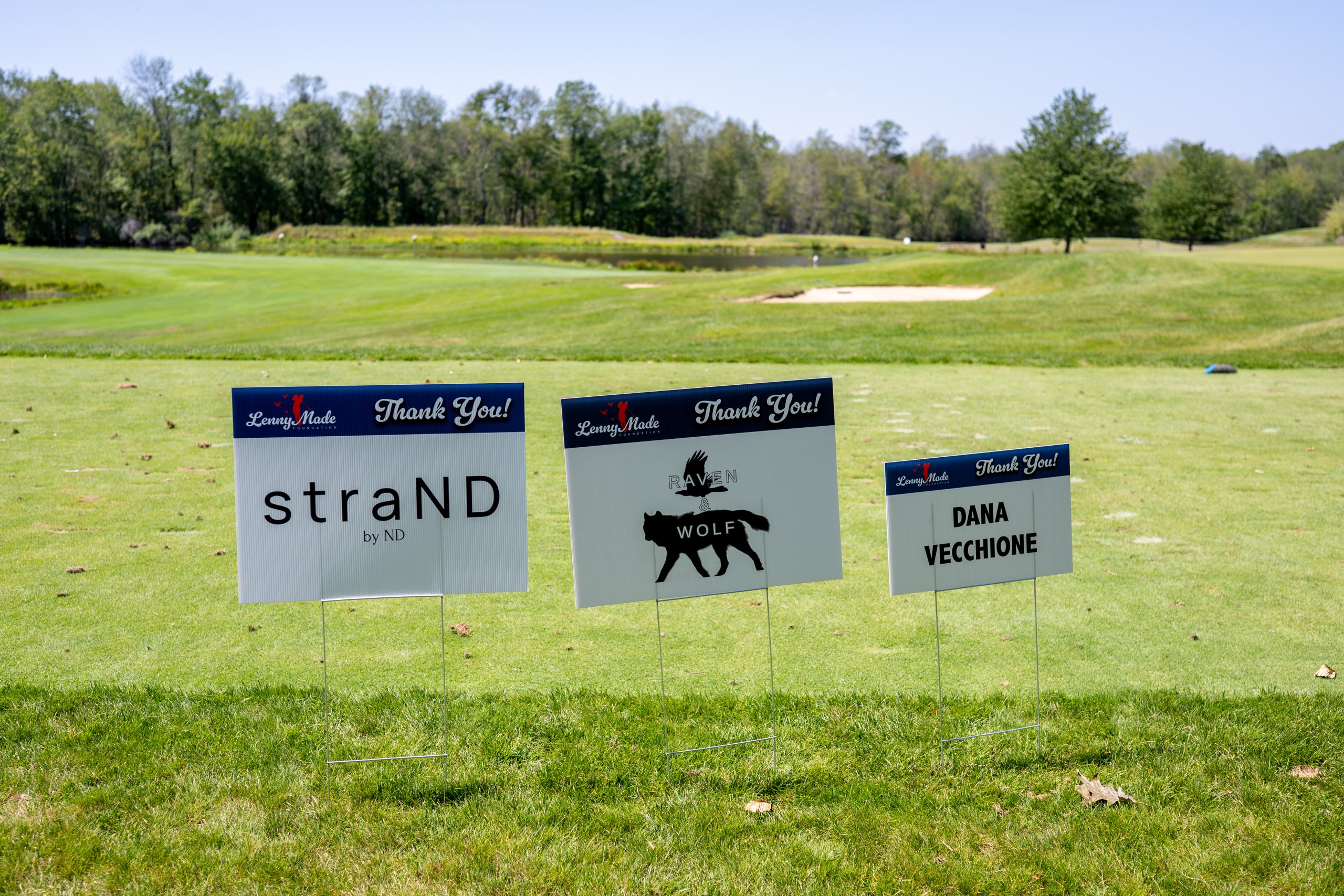 Three LennyMade Foundation sponsor signs at a tee: straND by ND, Raven and Wolf, and Dana Vecchione.