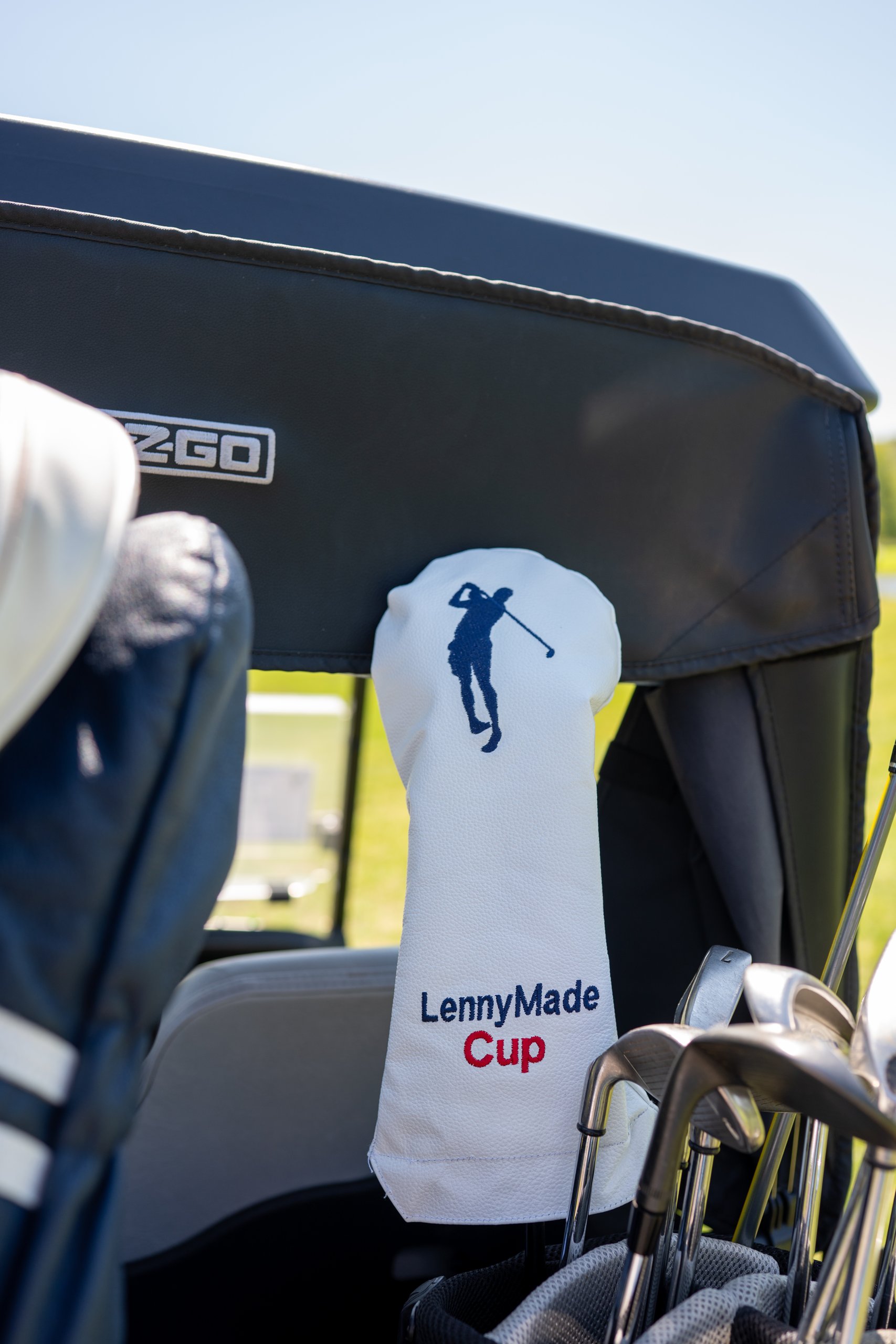 A white LennyMade Cup driver headcover with the navy golfer logo tucked in a bag on an E-Z-GO cart.