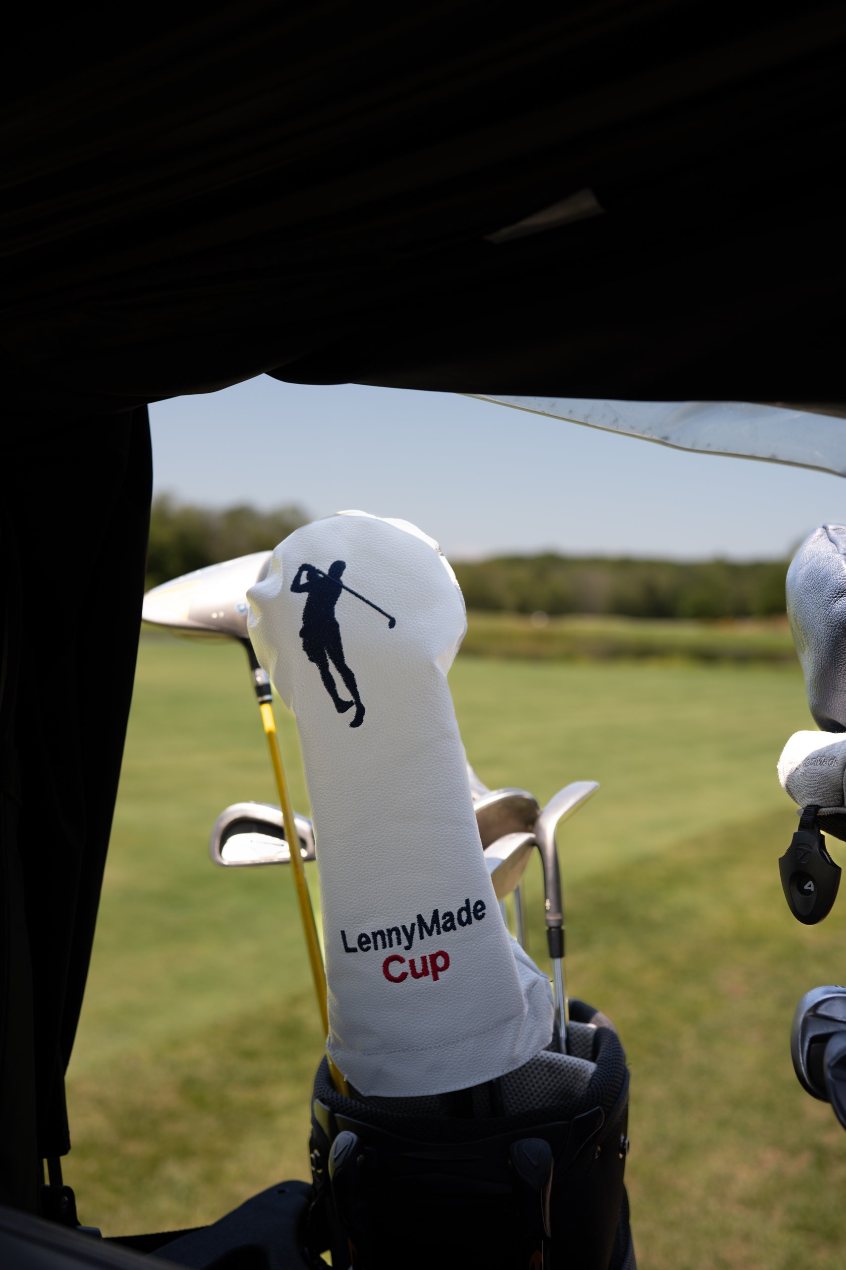 View from inside a cart of a white LennyMade Cup driver headcover in the bag, the fairway beyond.