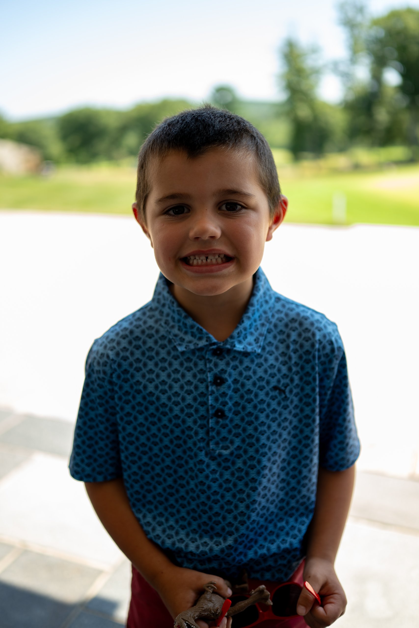 A young boy in a blue patterned polo smiling on the clubhouse patio.
