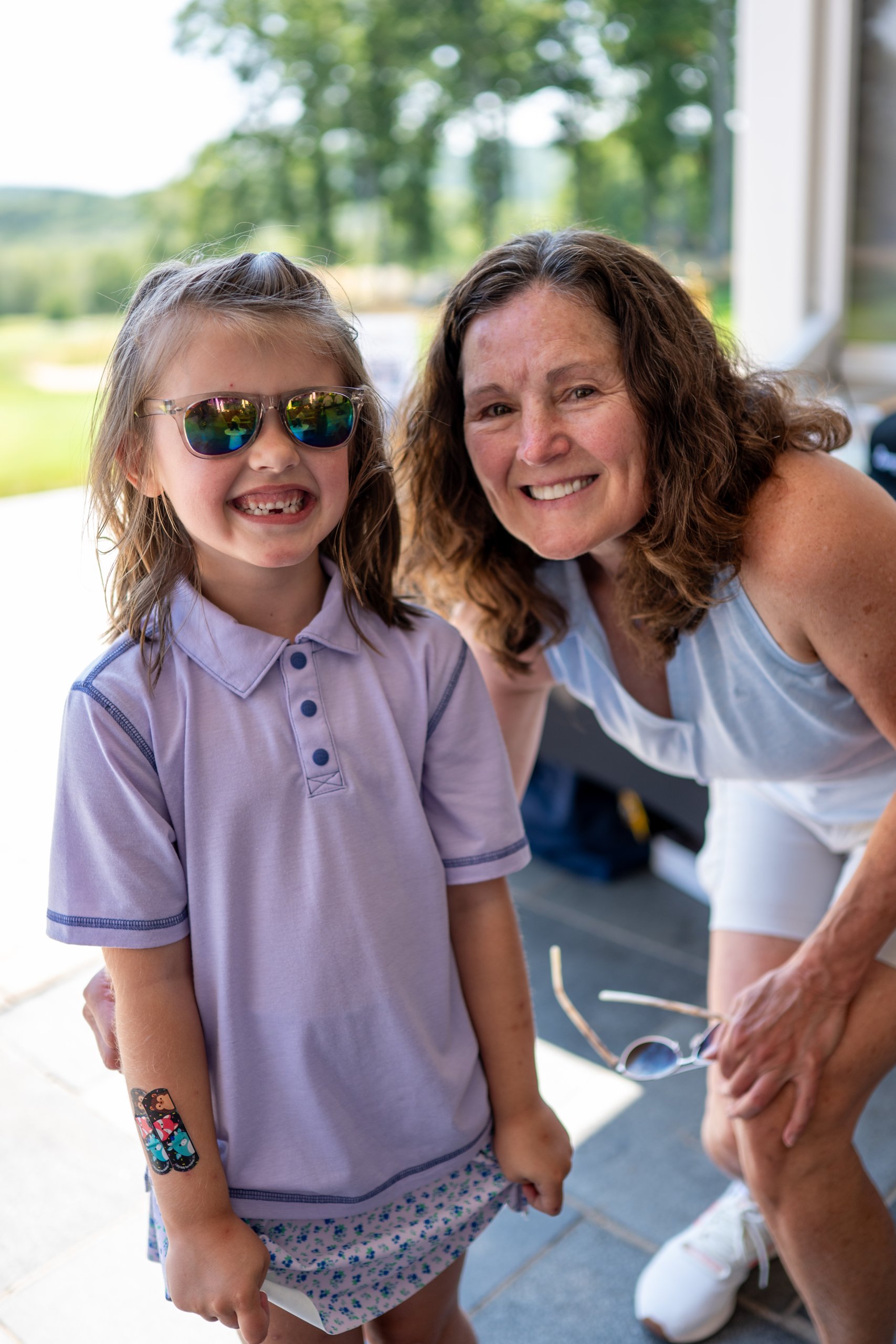A young girl in sunglasses smiling next to a woman on the clubhouse patio.