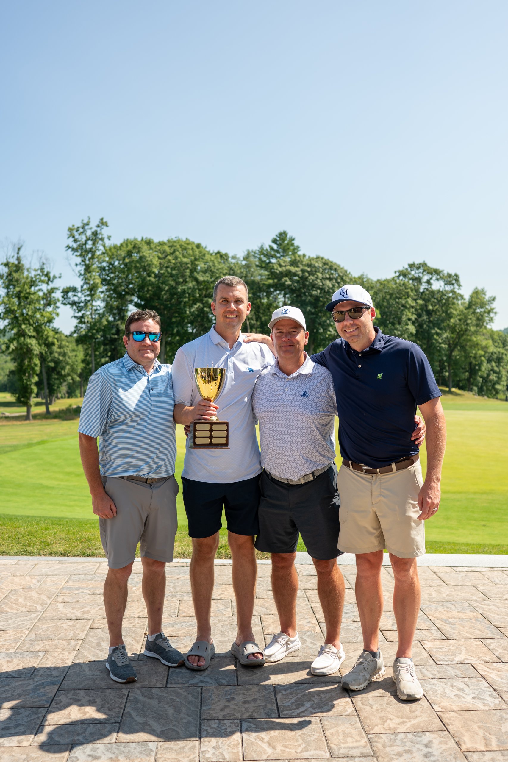 The winning foursome of four men posing with the gold LennyMade Cup trophy on the patio.