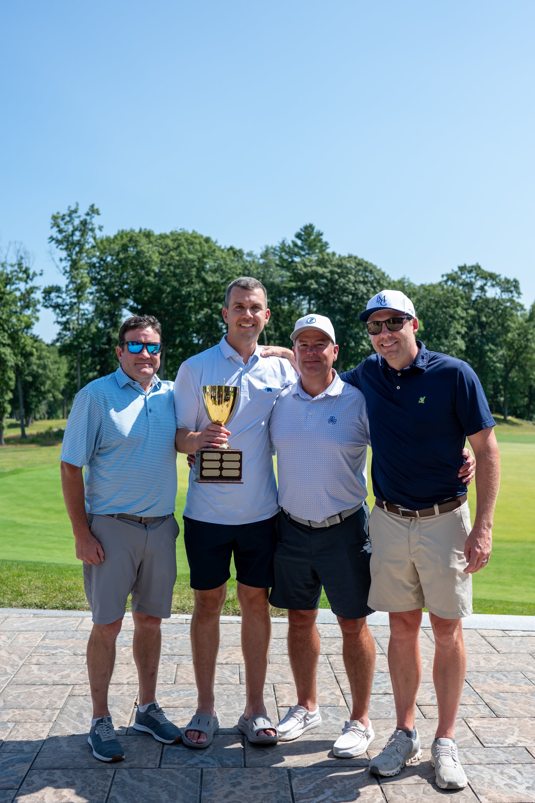 The winning team posing together with the LennyMade Cup trophy, the course behind them.