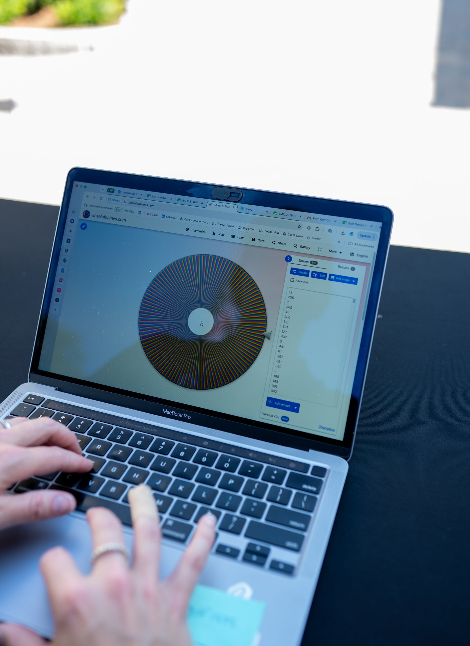 Over-the-shoulder view of a laptop showing a wheelofnames.com raffle wheel loaded with entries.