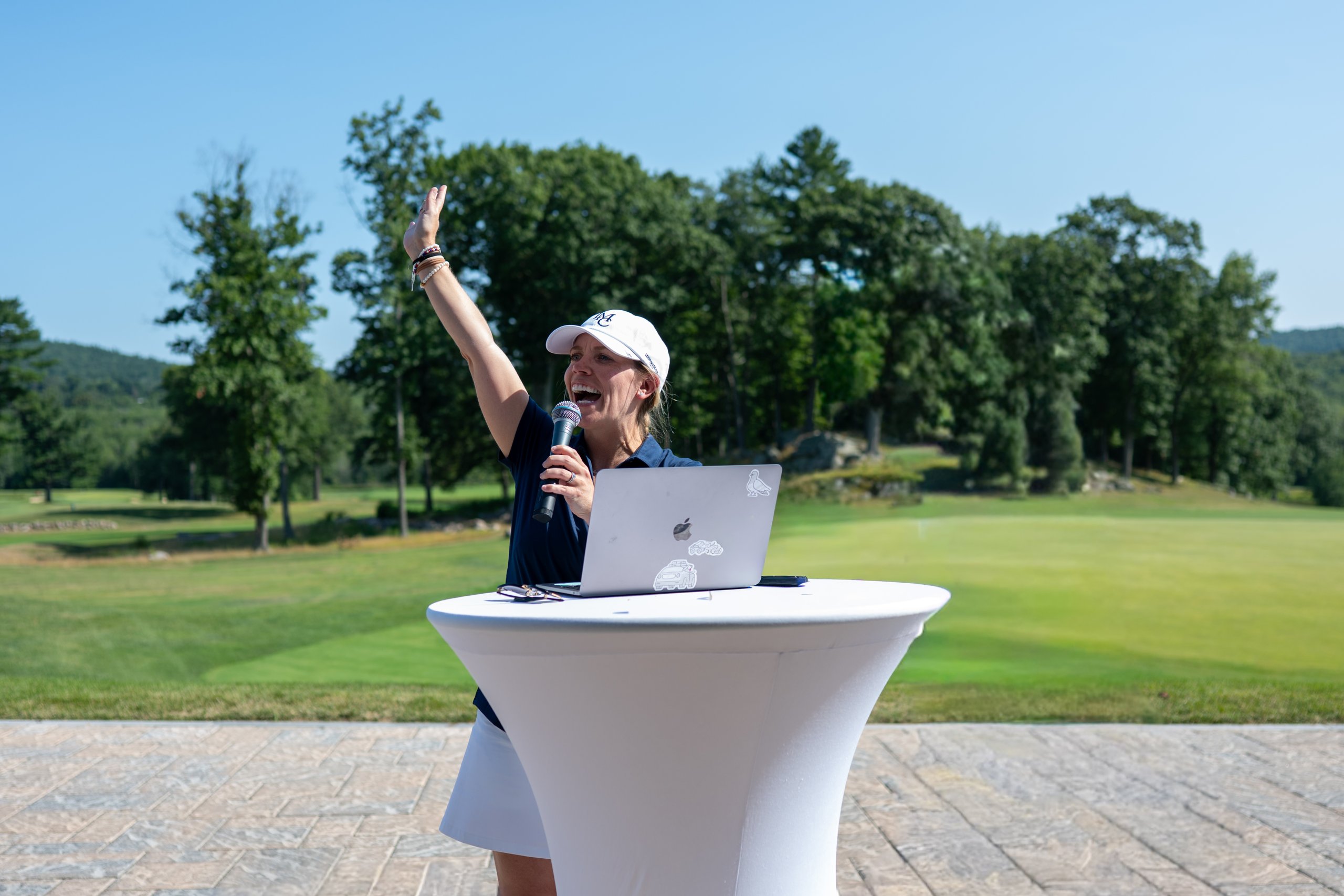 Event host raising her arm as she addresses the crowd with a microphone at the podium table.