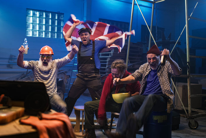 A group of actors dressed as workers celebrating with a Union Jack flag