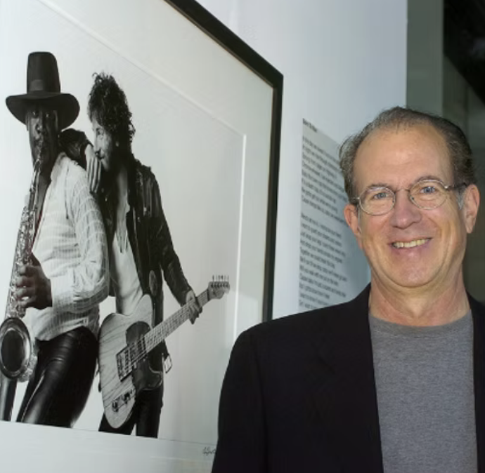 Eric Meola smiling beside a black-and-white photography of Born to Run cover images he shot. Text visible on wall. 