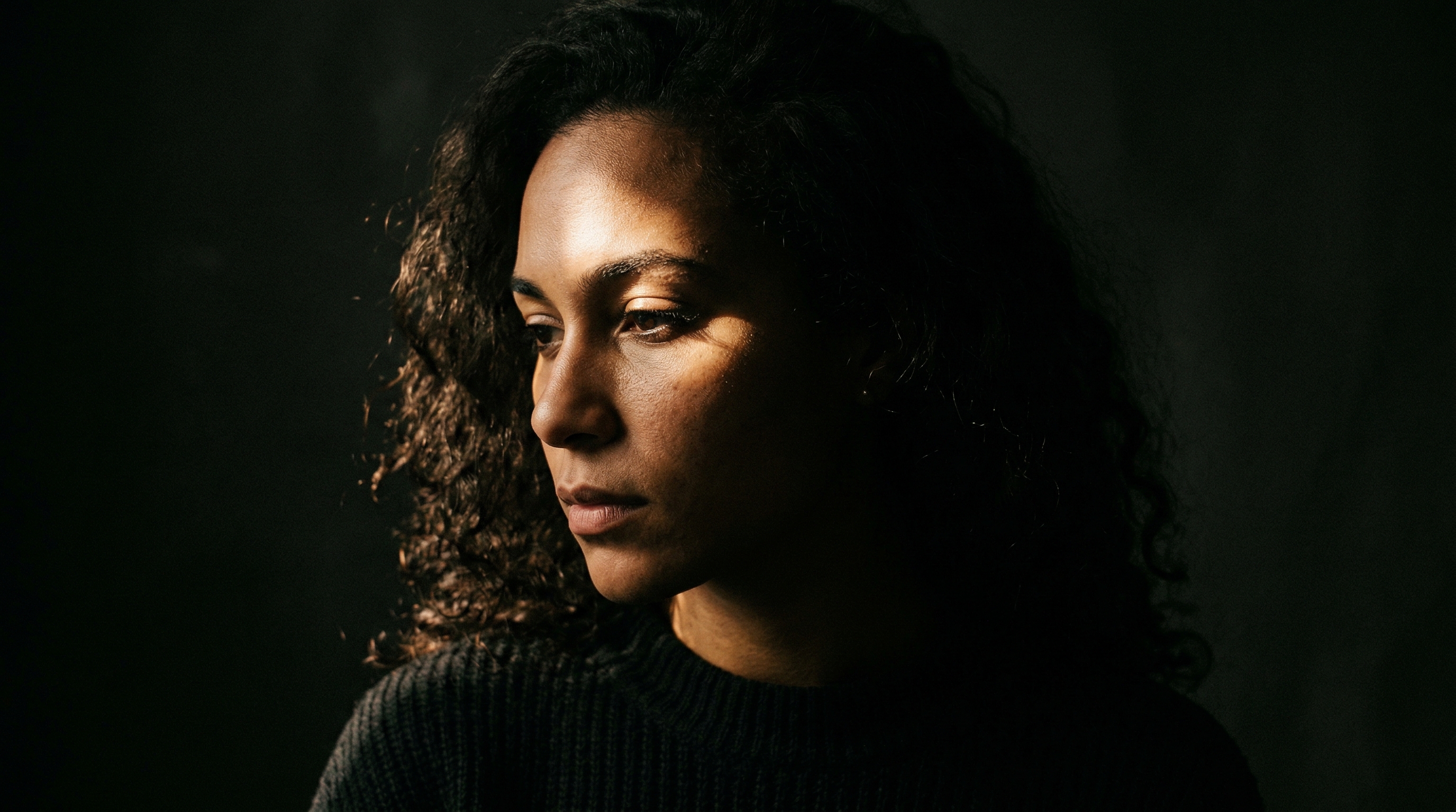 A dramatic chiaroscuro portrait showing intense contrast between light and shadow on a person's face, demonstrating the Renaissance-inspired single-light technique achievable with a desk lamp and aluminum foil snoot