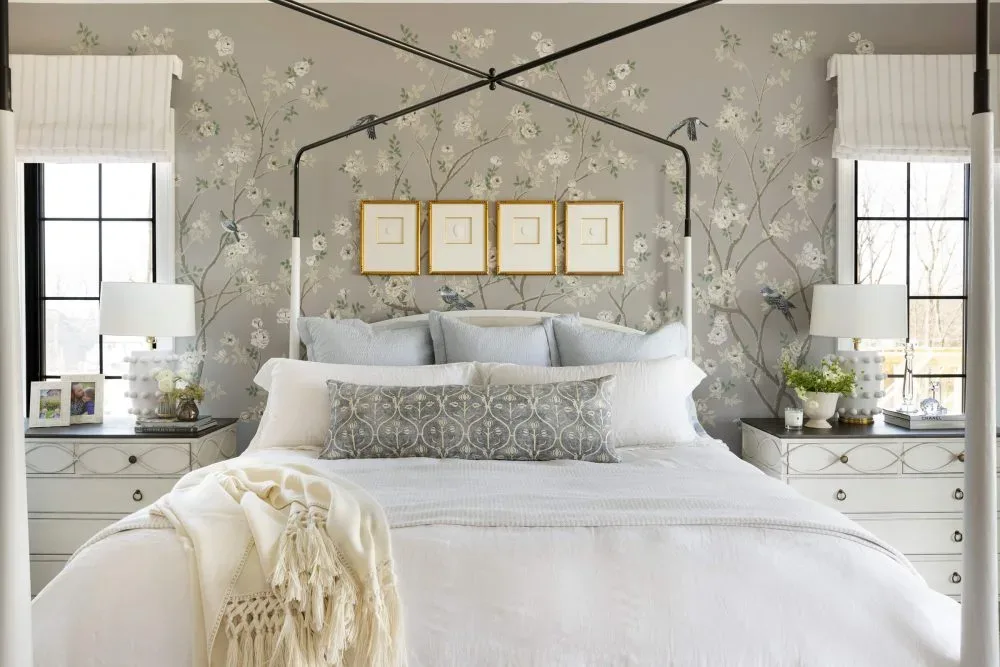 Serene bedroom featuring a four-poster bed with white bedding, floral wallpaper accent wall, matching nightstands with white lamps, and soft neutral decor, designed by Decozie designer Nicole W.