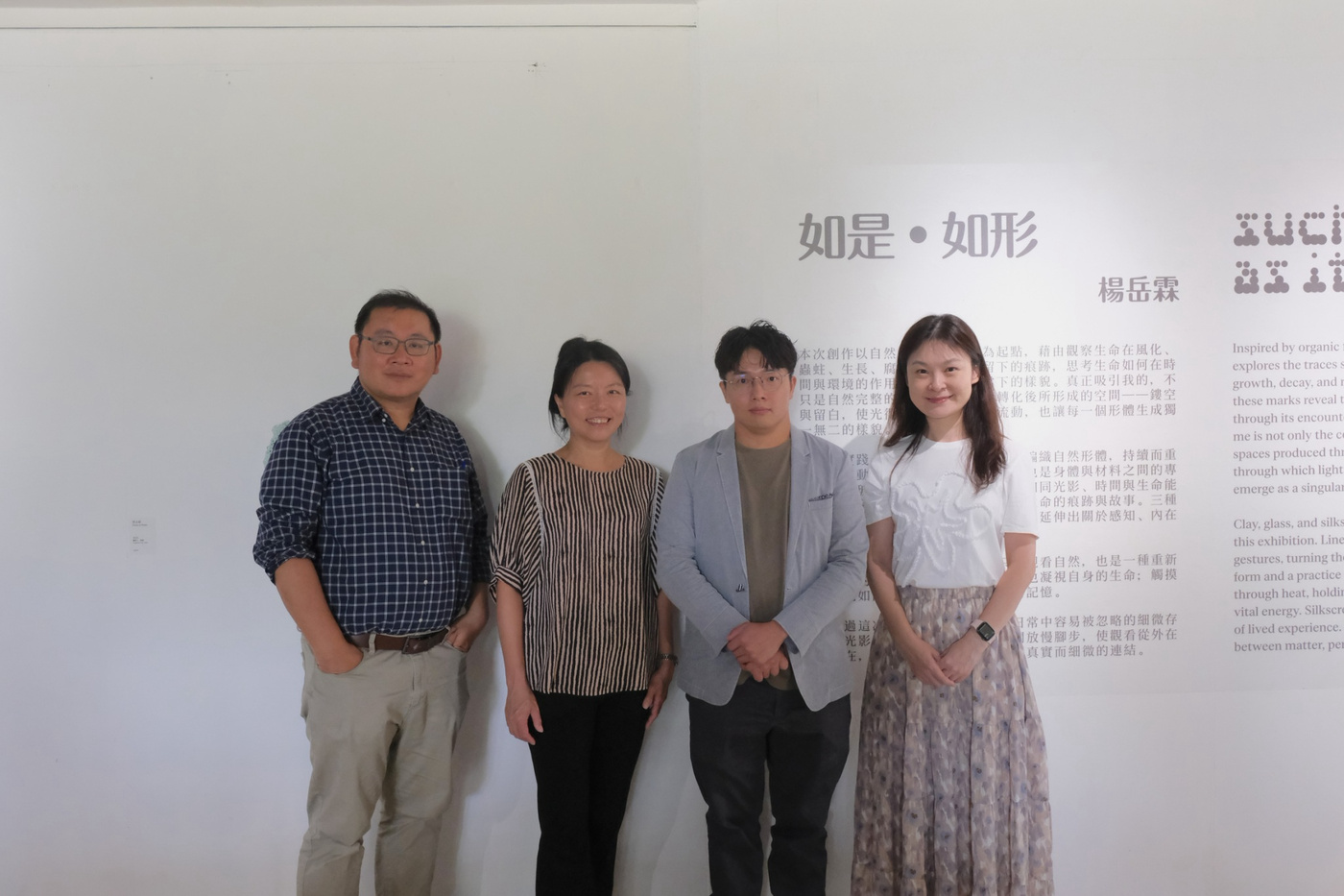 四個人站在牆面面板前合照，面板標題為「如是·如形」。面板上包含中英文雙語文本，說明藝術作品的概念。